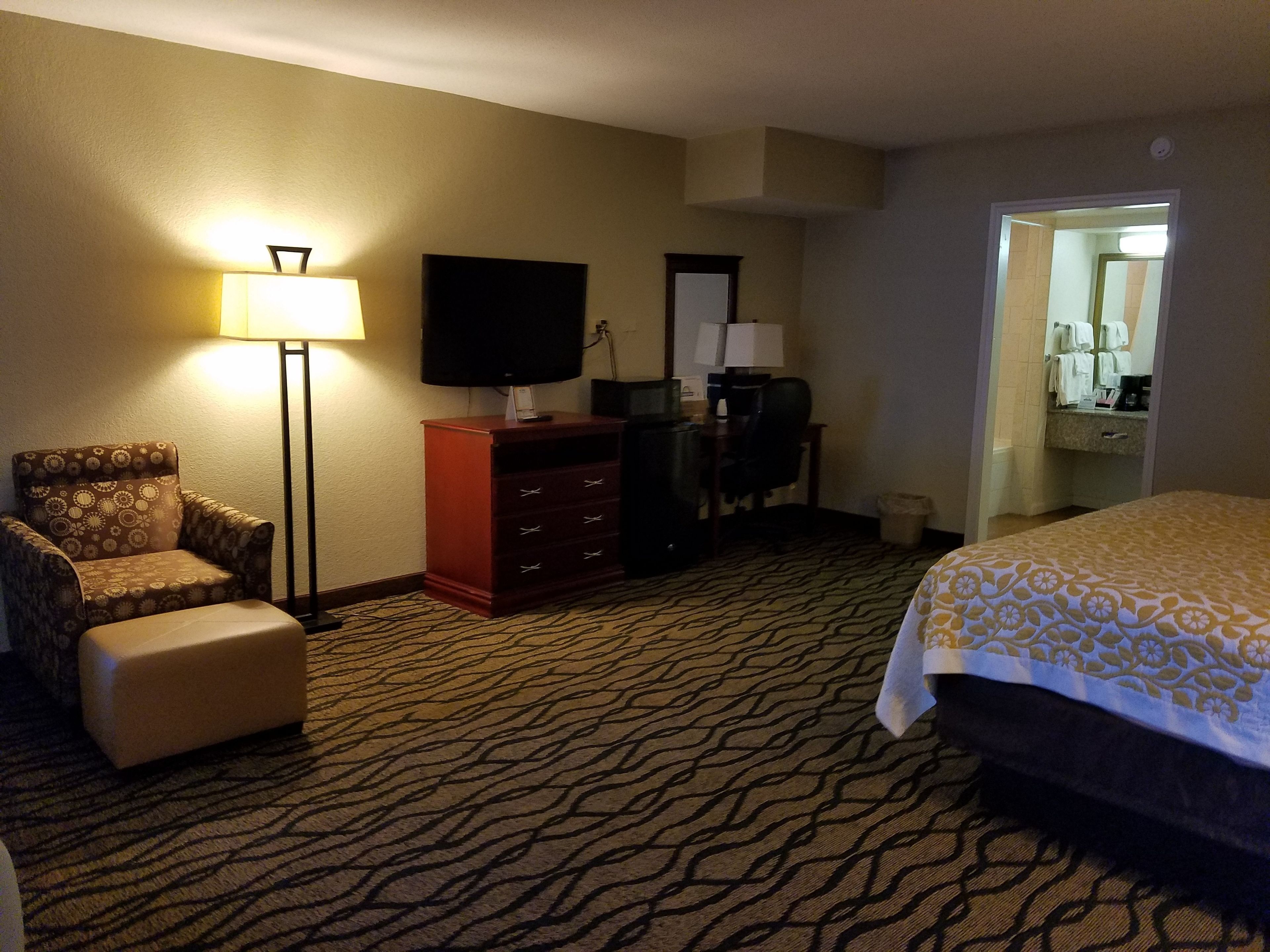 Habitación de hotel con cama, sillón, escritorio, televisor y baño visible a través de una puerta abierta.