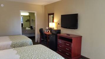 Et hotelværelse med to senge, et skrivebord med stol, et fjernsyn og en kommode.