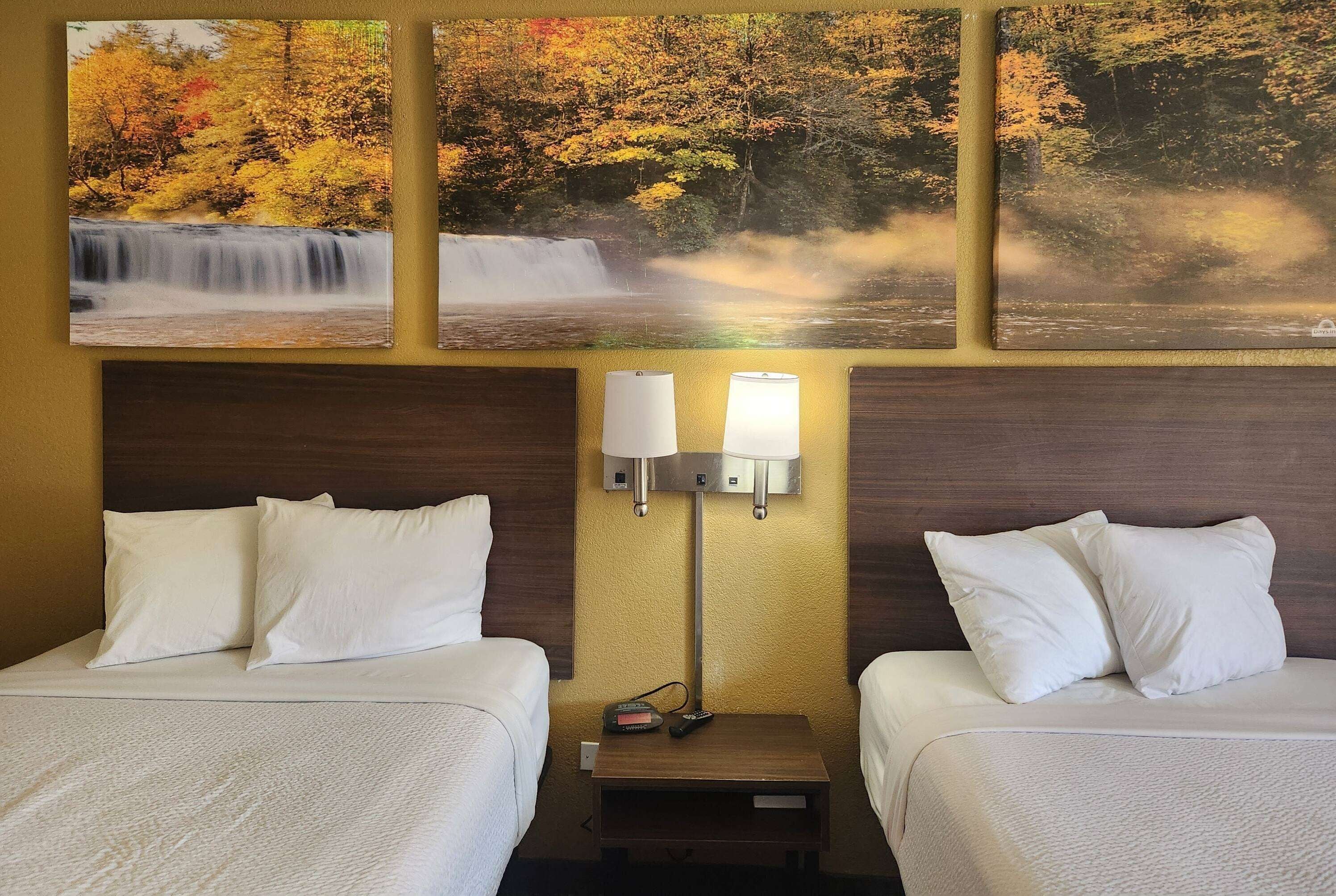 A hotel room with two beds, a nightstand with a lamp, and three framed pictures of waterfalls.