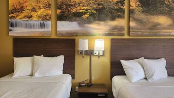 A hotel room with two beds, a nightstand with a lamp, and three framed pictures of waterfalls.