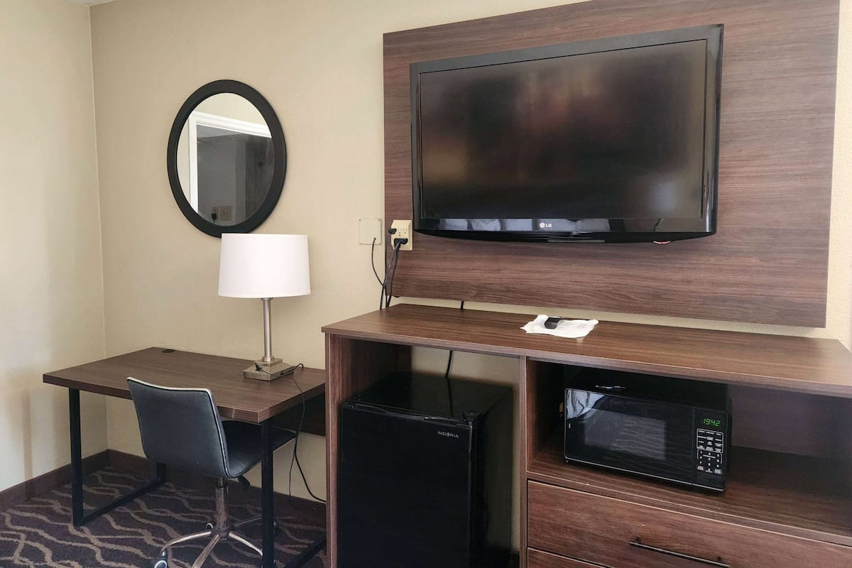 Habitación de hotel con escritorio, silla, televisor, microondas y espejo.