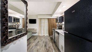 Una cocina moderna con un refrigerador negro, gabinetes blancos y piso de madera.