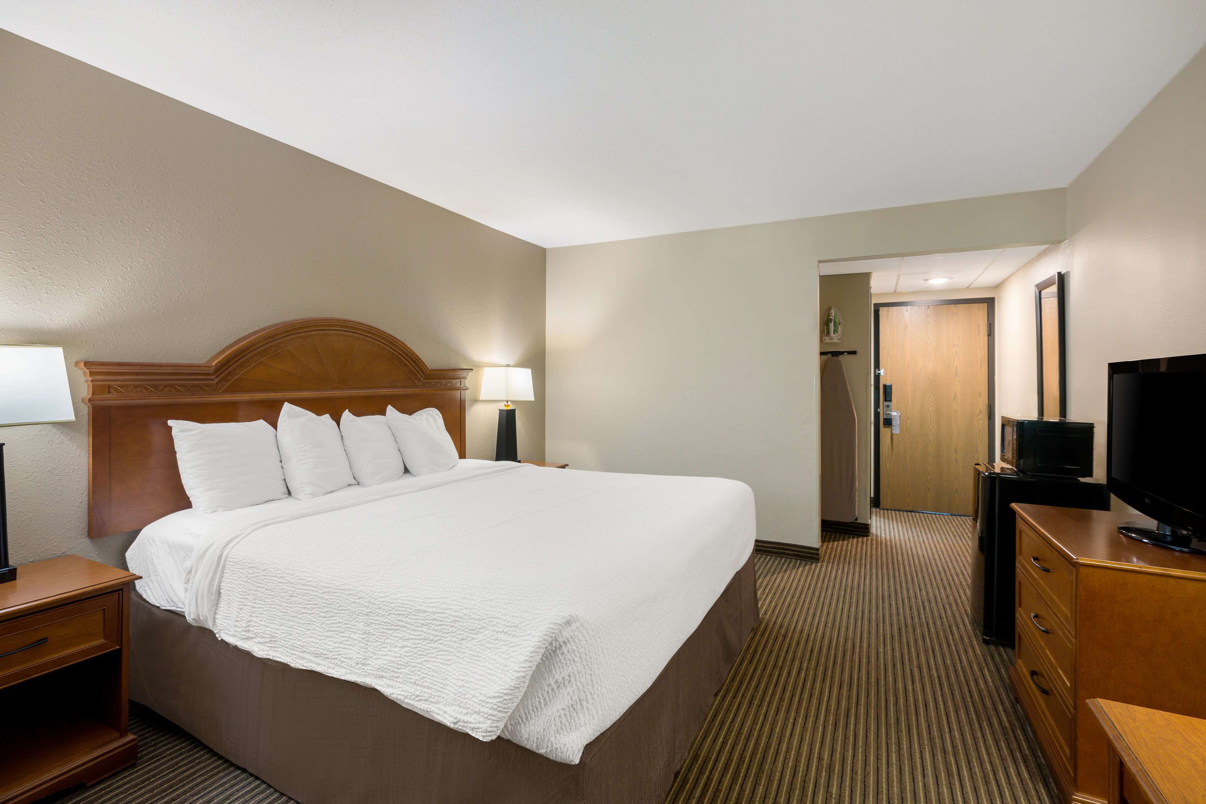 Una habitación de hotel con una cama grande, un televisor, una cómoda y una lámpara.
