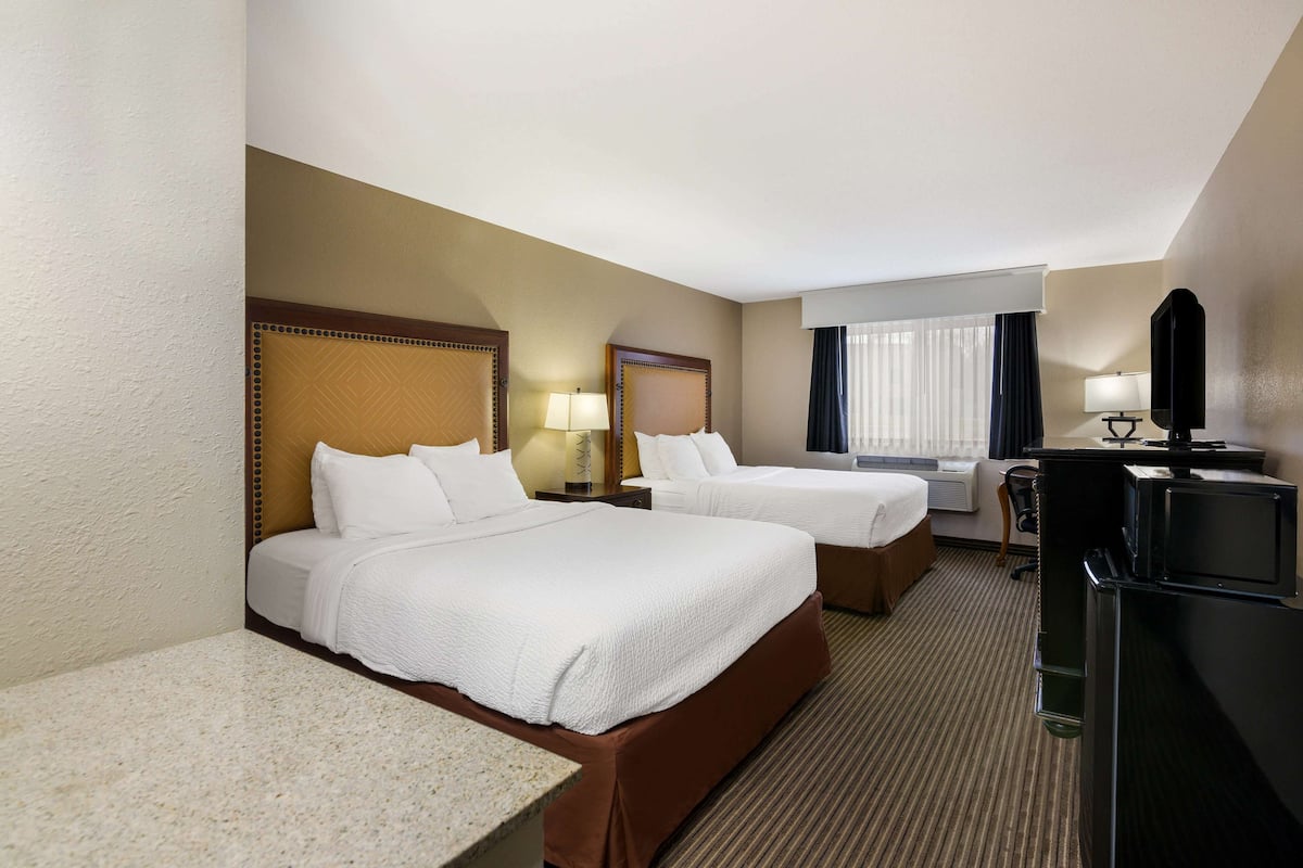 A hotel room with two beds, a desk, a TV, and a window with curtains.