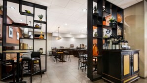 Un restaurante moderno con una zona de bar, diferentes disposiciones de asientos y estantes decorativos.