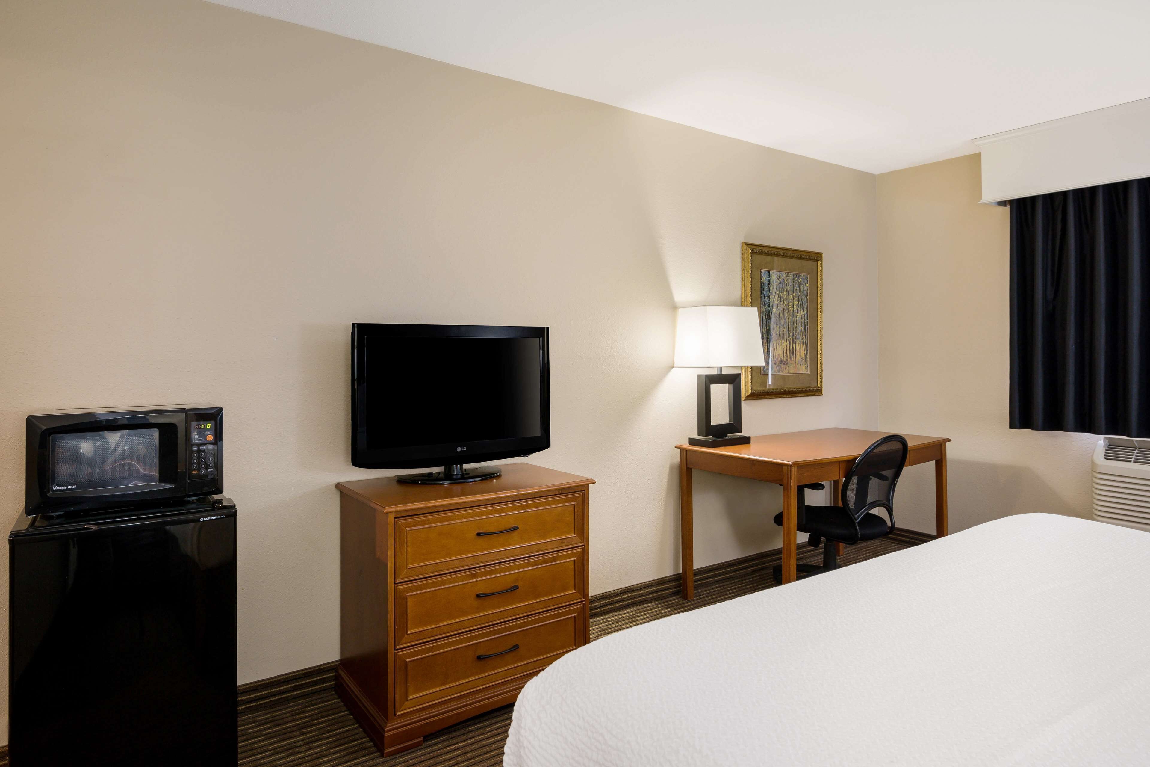 Ein Hotelzimmer mit Bett, Schreibtisch mit Stuhl, Fernseher, Mikrowelle und Lampe.