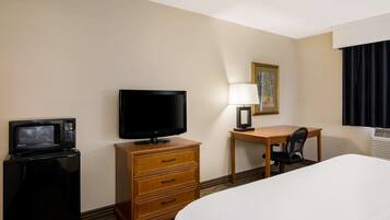 Ein Hotelzimmer mit Bett, Schreibtisch mit Stuhl, Fernseher, Mikrowelle und Lampe.