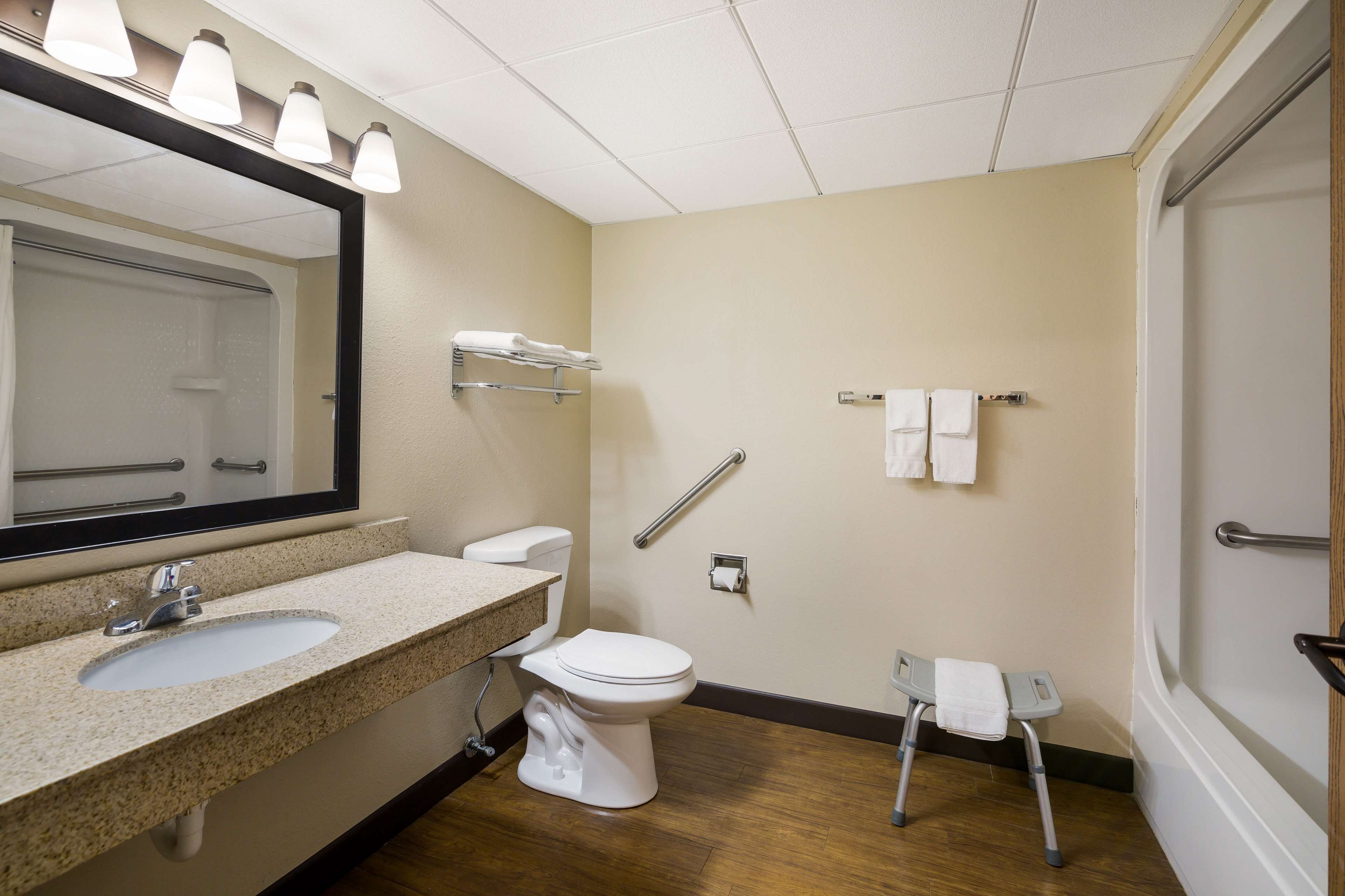 Baño con lavamanos, inodoro y un asiento accesible para sillas de ruedas.