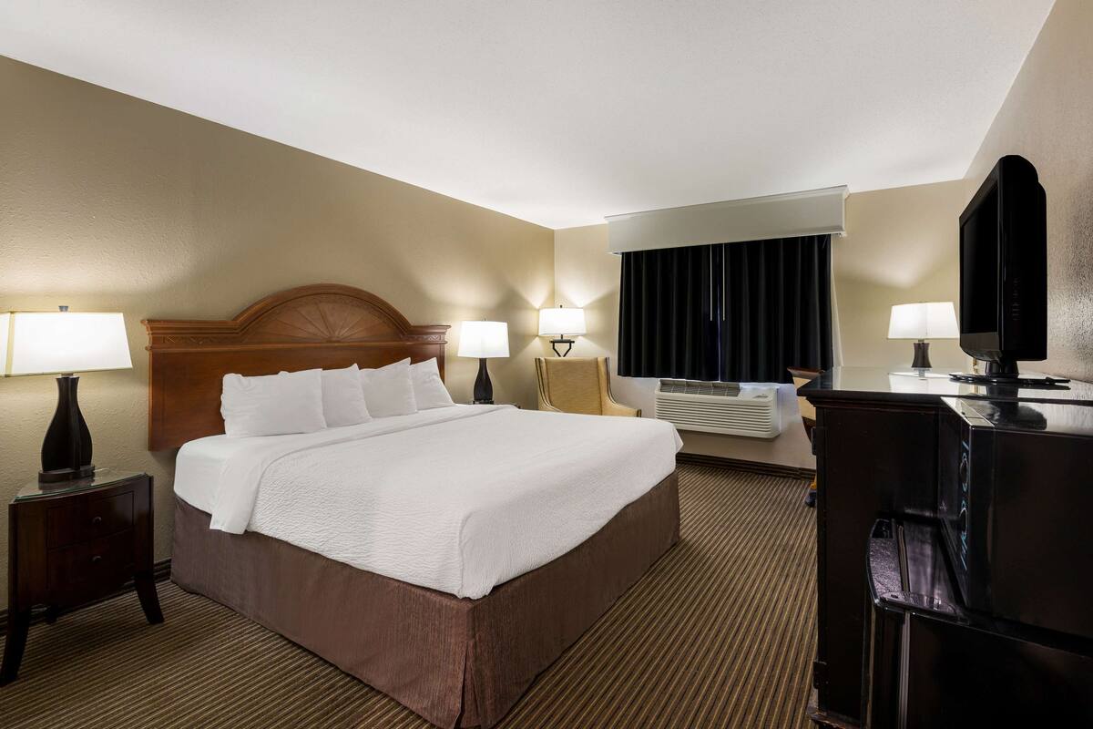 A hotel room with a large bed, two bedside tables with lamps, a TV, and an air conditioning unit.