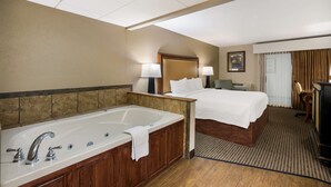 Habitación de hotel con una bañera grande, una cama doble, una mesita de noche, una lámpara y una silla.