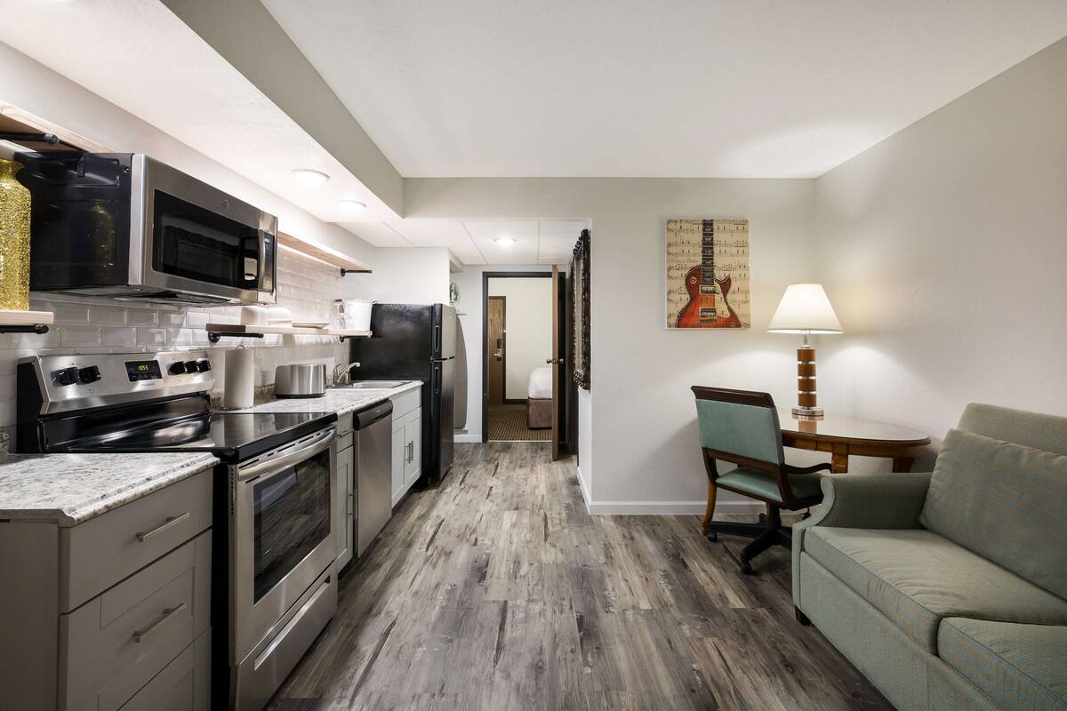 A modern kitchen with stainless steel appliances, a wooden floor, and a green sofa in the living area.