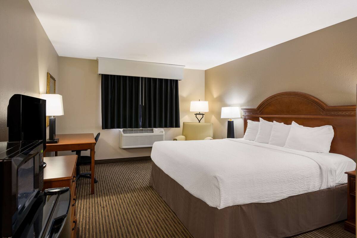A hotel room with a large bed, a desk with a chair, a television, and two lamps.