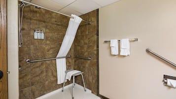 Een badkamer met een douche, handgrepen, een opstapje en een handdoekhouder.