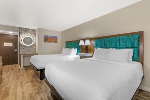 Une chambre d’hôtel avec deux lits, un miroir rond, un tableau et un plancher en bois.