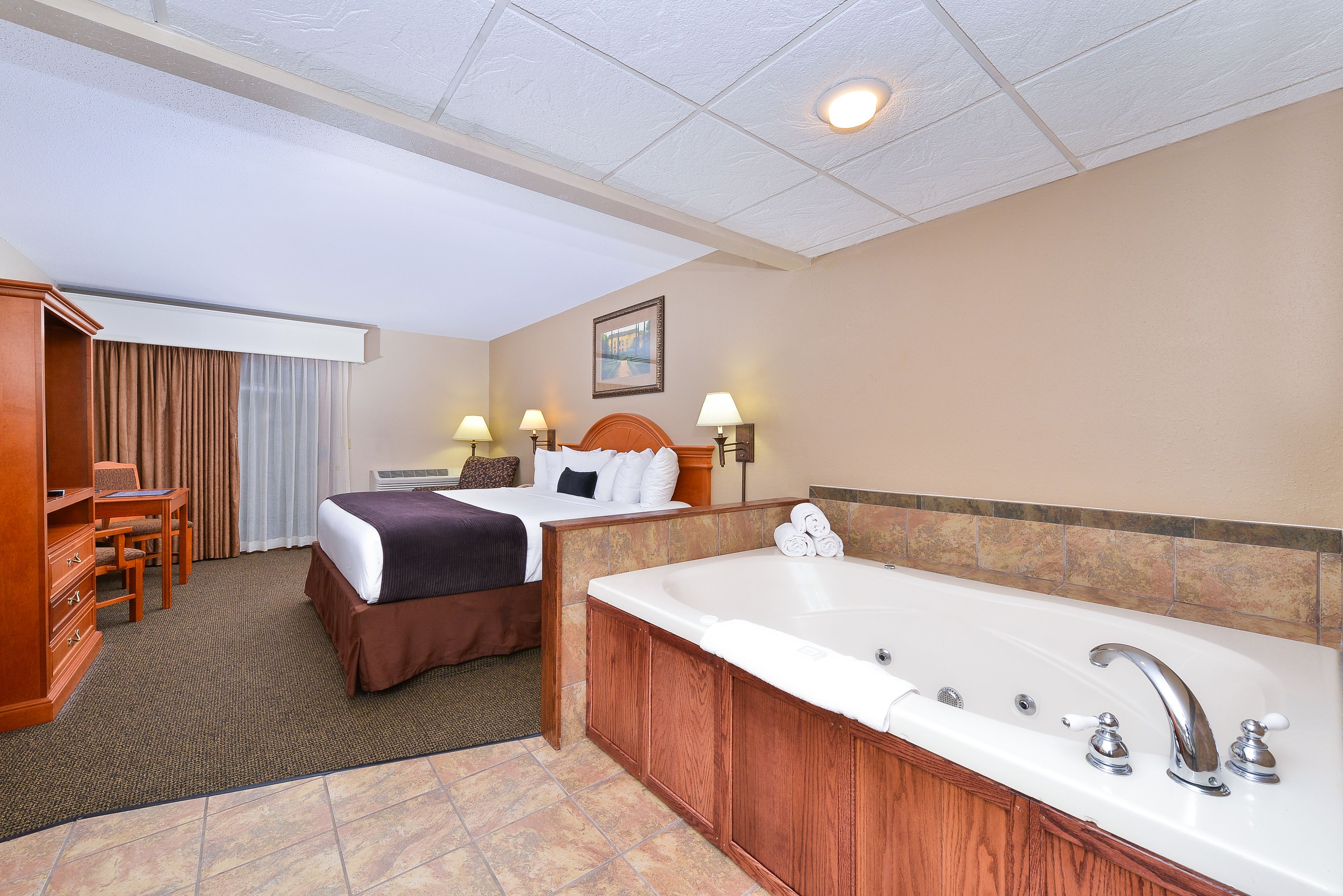 A hotel room with a bed, a desk, a chair, a bathroom with a bathtub, and a shower.