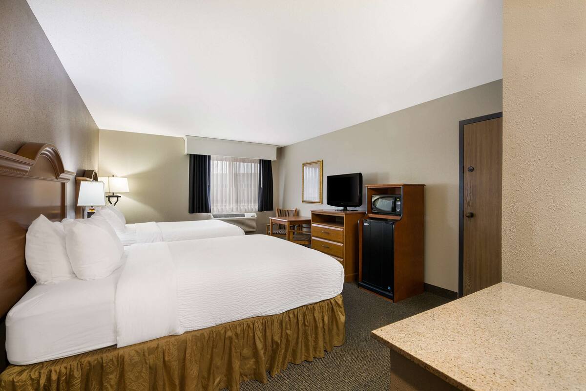 A hotel room with two beds, a desk, a television, and a minibar.