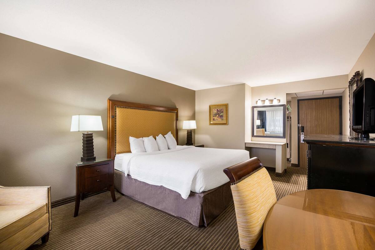 A hotel room with a large bed, bedside tables with lamps, a desk with a chair, a television, and a mirror.