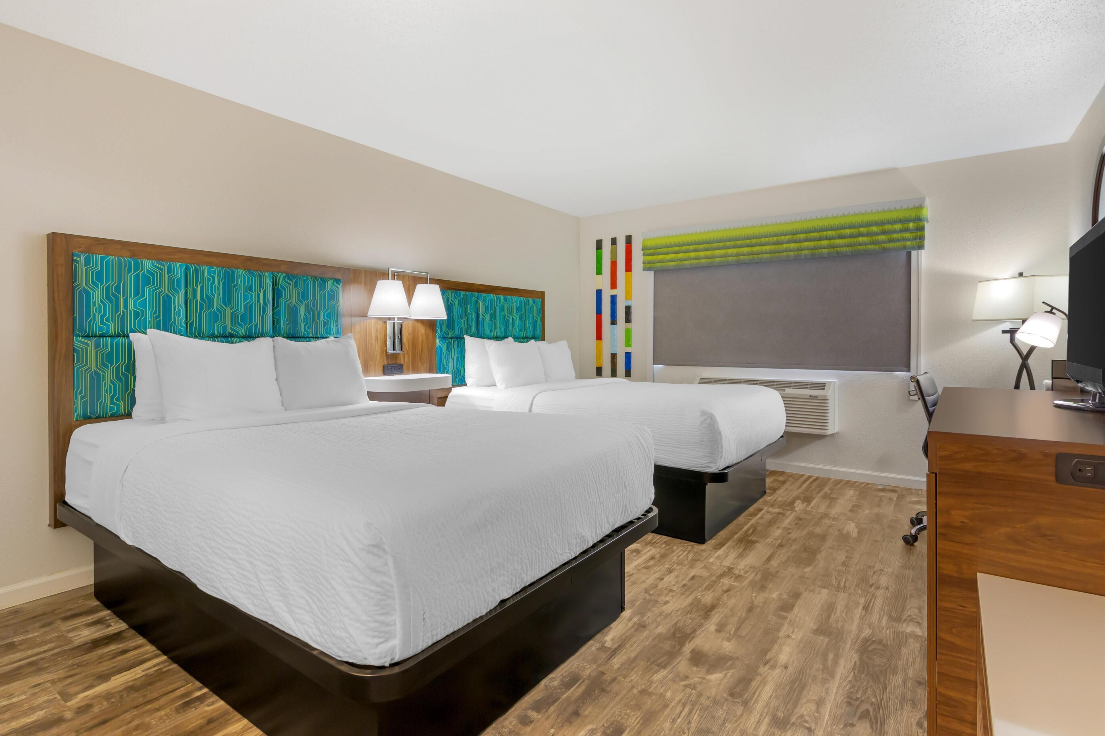 Habitación de hotel con una cama grande, mesitas de noche, televisor y ventana con cortinas.