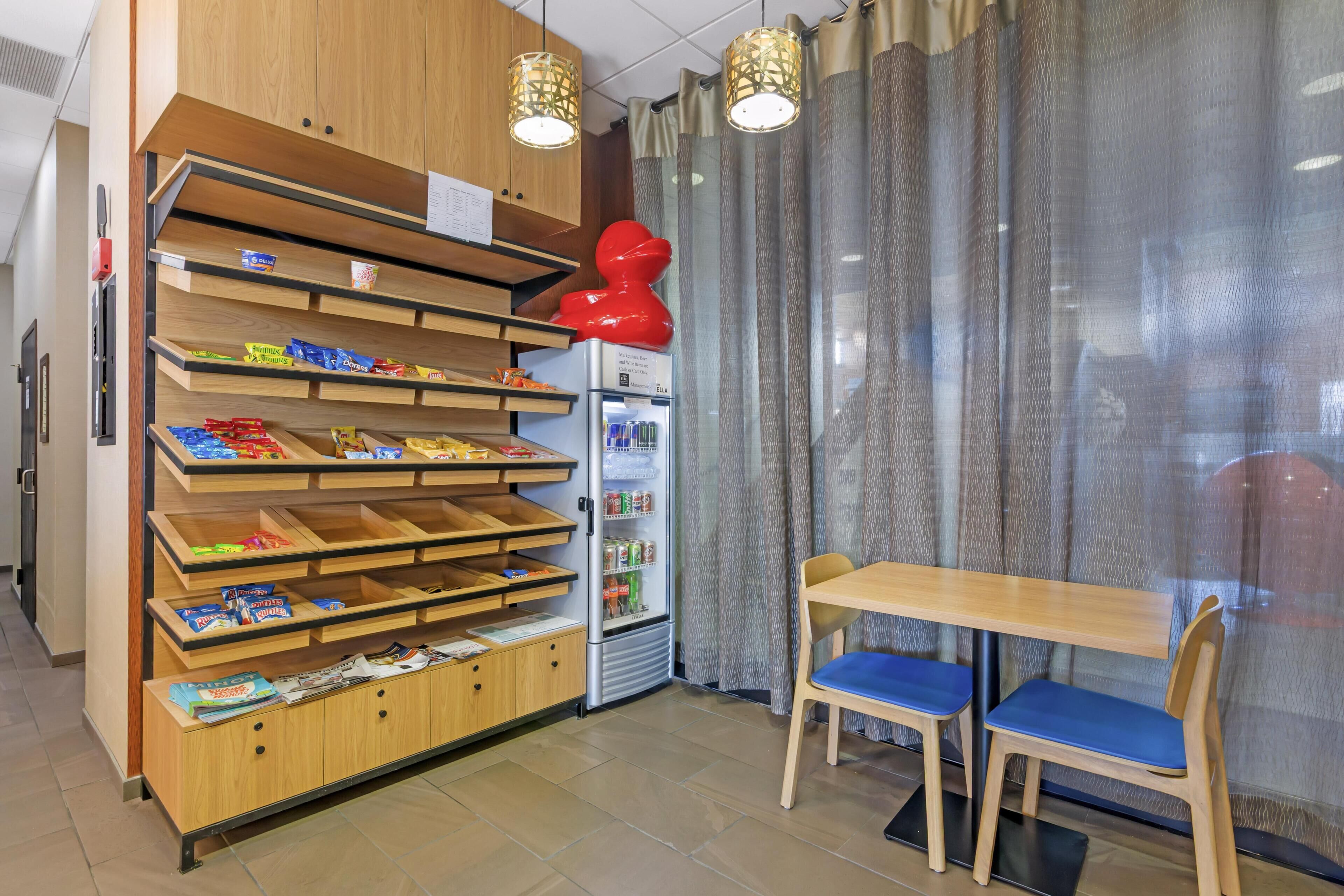 Eine kleine Gastronomieeinheit mit Holzböden, gut sortiert mit verschiedenen Snacks, einem Getränkekühlschrank und einer Sitzecke mit Tisch und Stühlen.