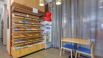 Eine kleine Gastronomieeinheit mit Holzböden, gut sortiert mit verschiedenen Snacks, einem Getränkekühlschrank und einer Sitzecke mit Tisch und Stühlen.