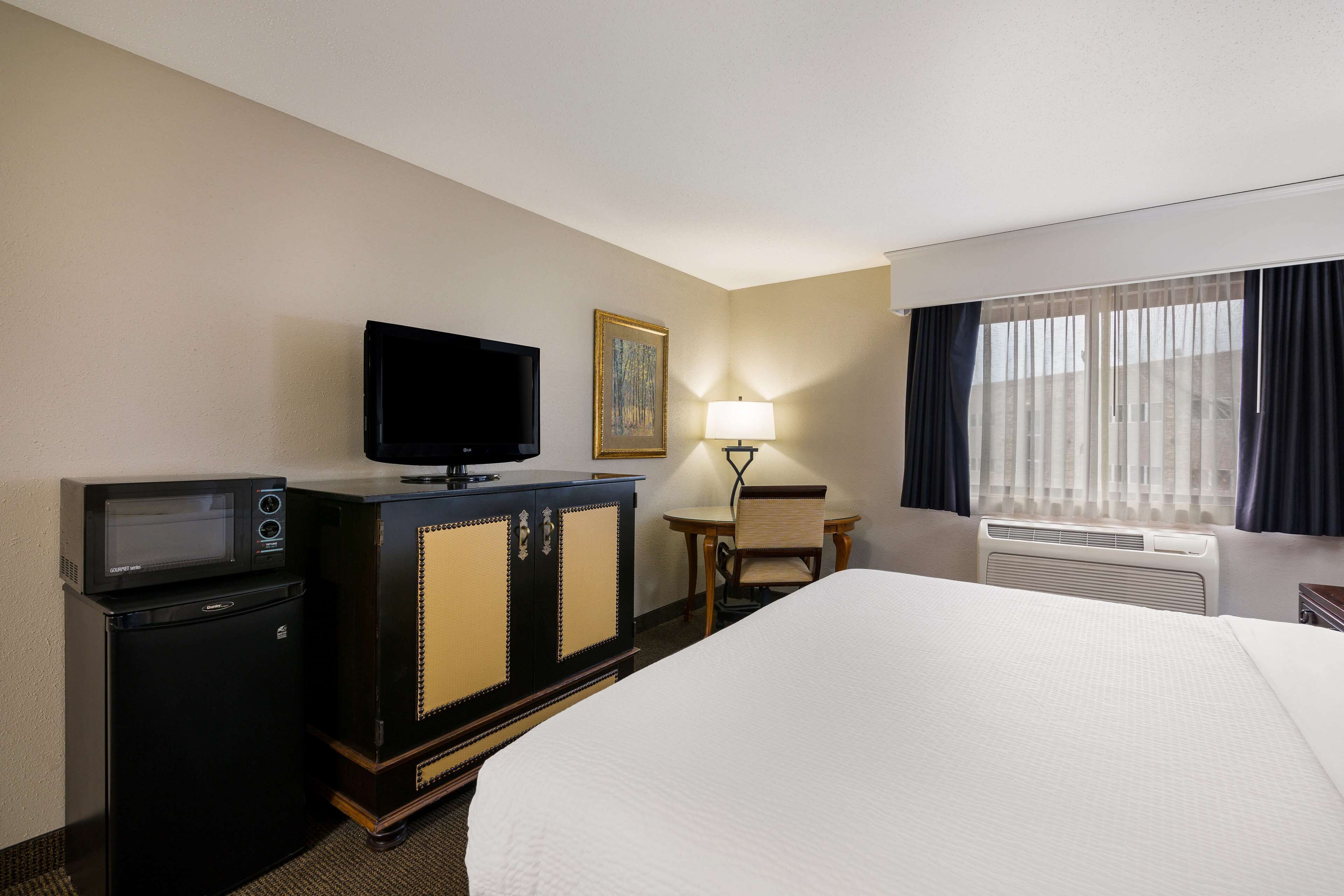A hotel room with a bed, a television, a minibar, a desk, and a window with curtains.