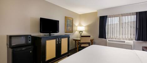 A hotel room with a bed, a television, a minibar, a desk, and a window with curtains.