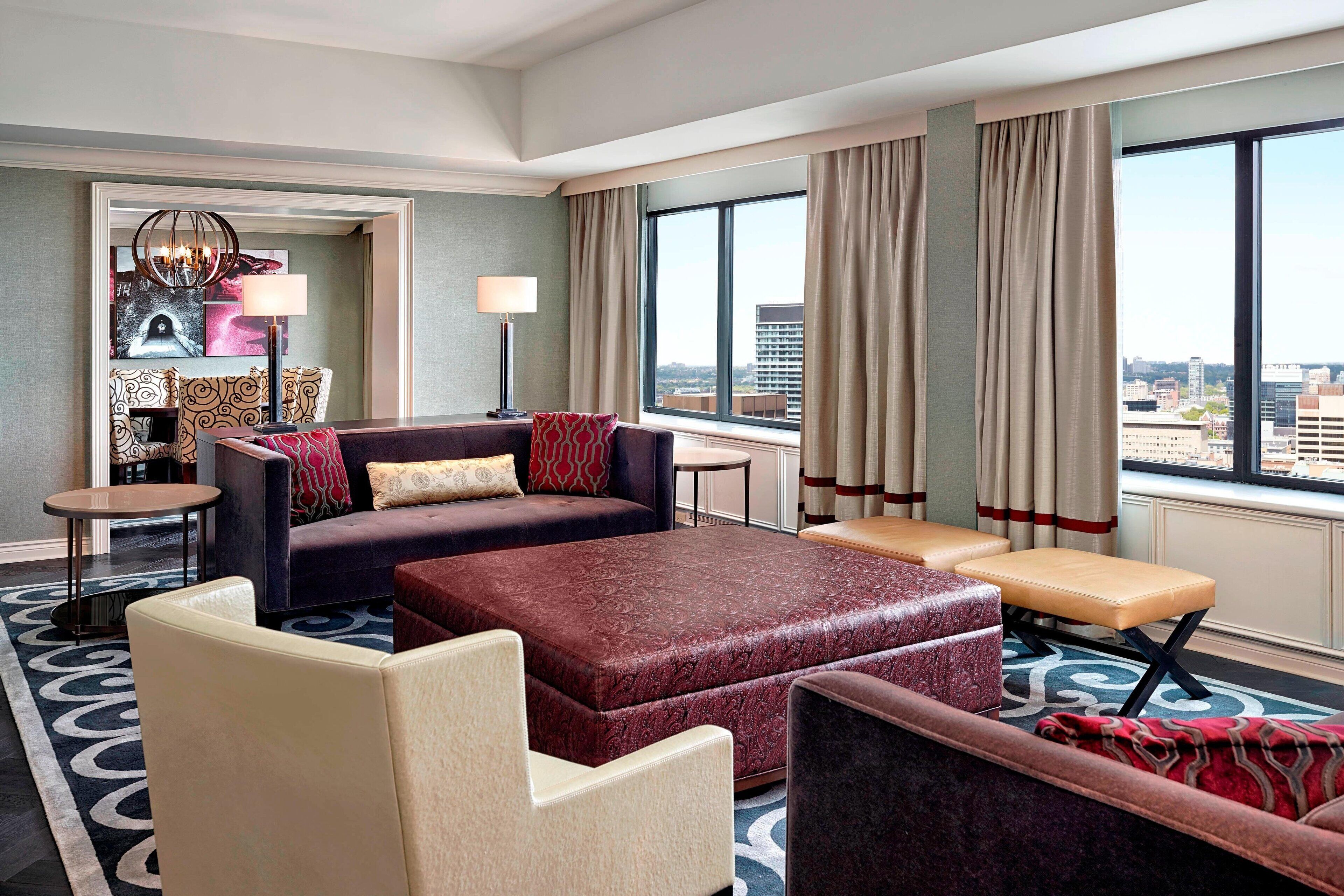 A modern hotel room with a sofa, armchair, ottoman, and a small table.