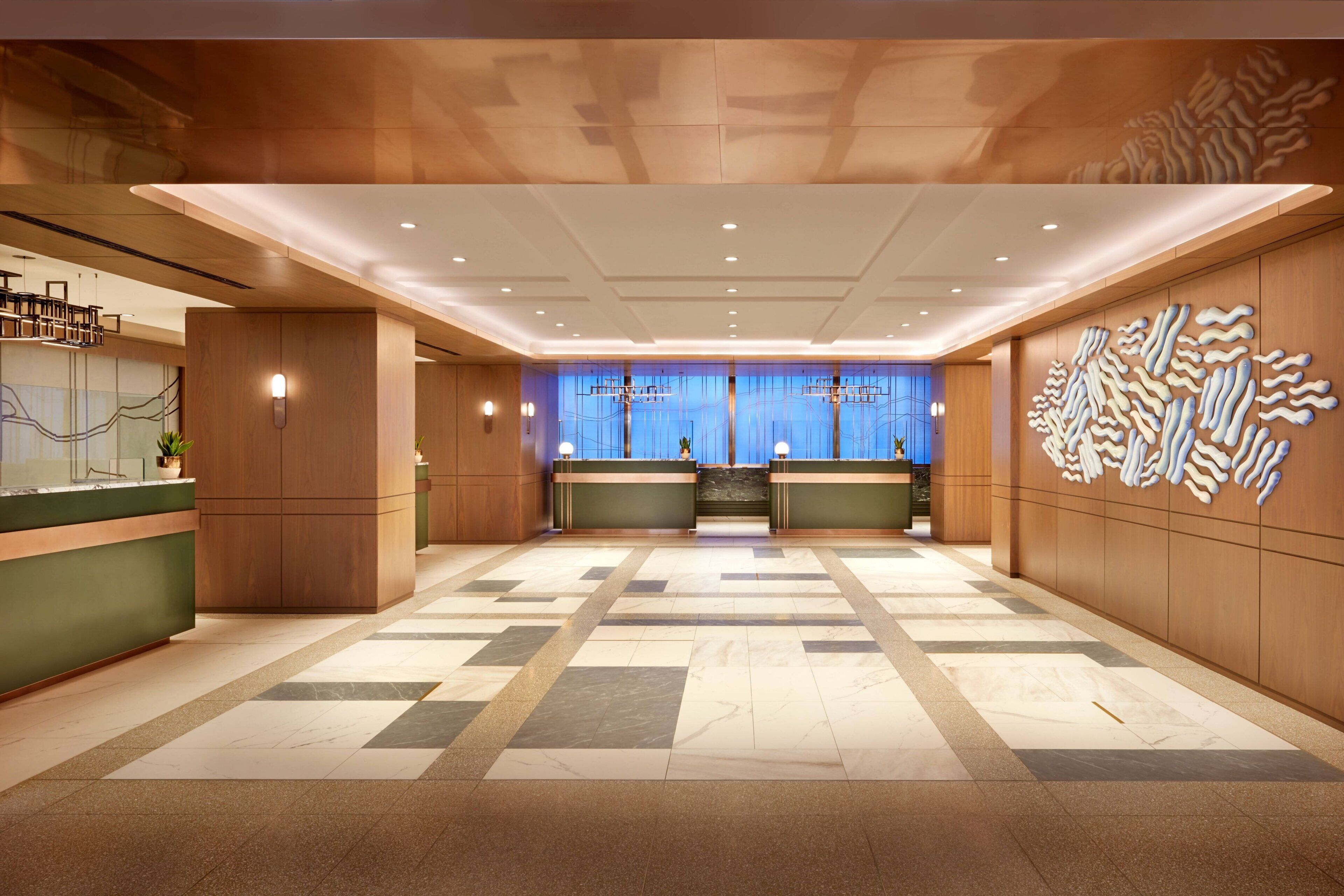 A hotel lobby with a reception desk, a blue wall with a decorative pattern, and a tiled floor.