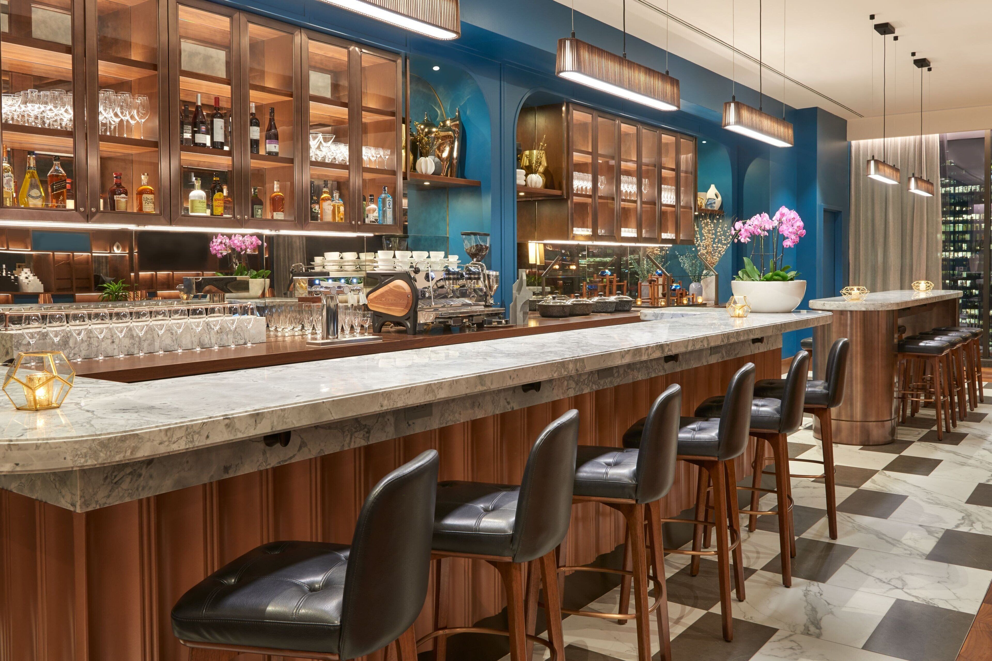 A bar area with a marble countertop, black leather bar stools, and a variety of bottles and glasses on shelves.