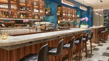 A bar area with a marble countertop, black leather bar stools, and a variety of bottles and glasses on shelves.