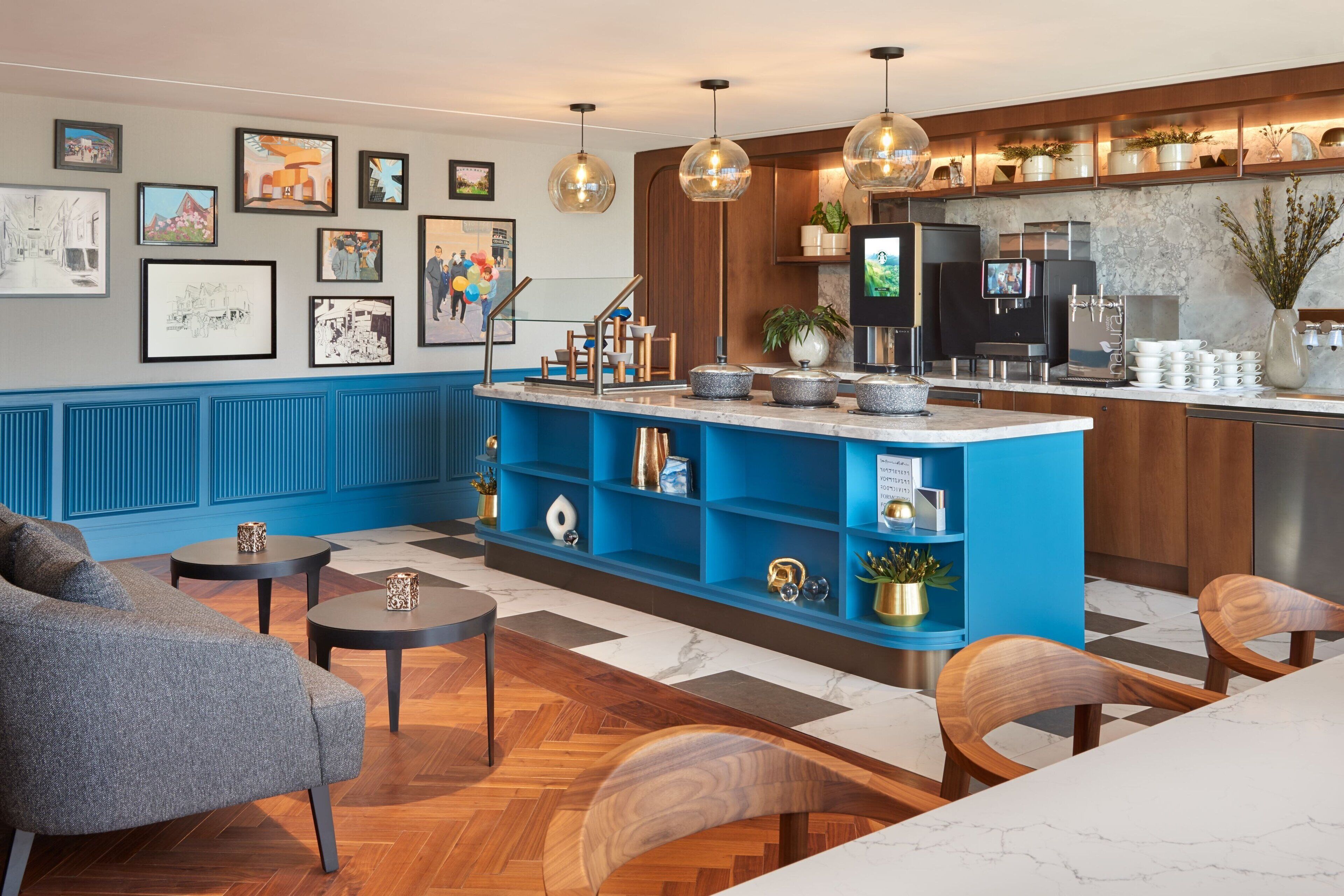 Een moderne hotellobby met een blauwe receptiebalie, houten stoelen, een bank en kunstwerken aan de muren.