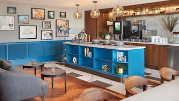 Een moderne hotellobby met een blauwe receptiebalie, houten stoelen, een bank en kunstwerken aan de muren.