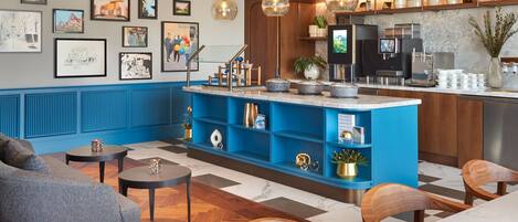 A modern hotel lobby with a blue reception desk, wooden chairs, a sofa, and artwork on the walls.