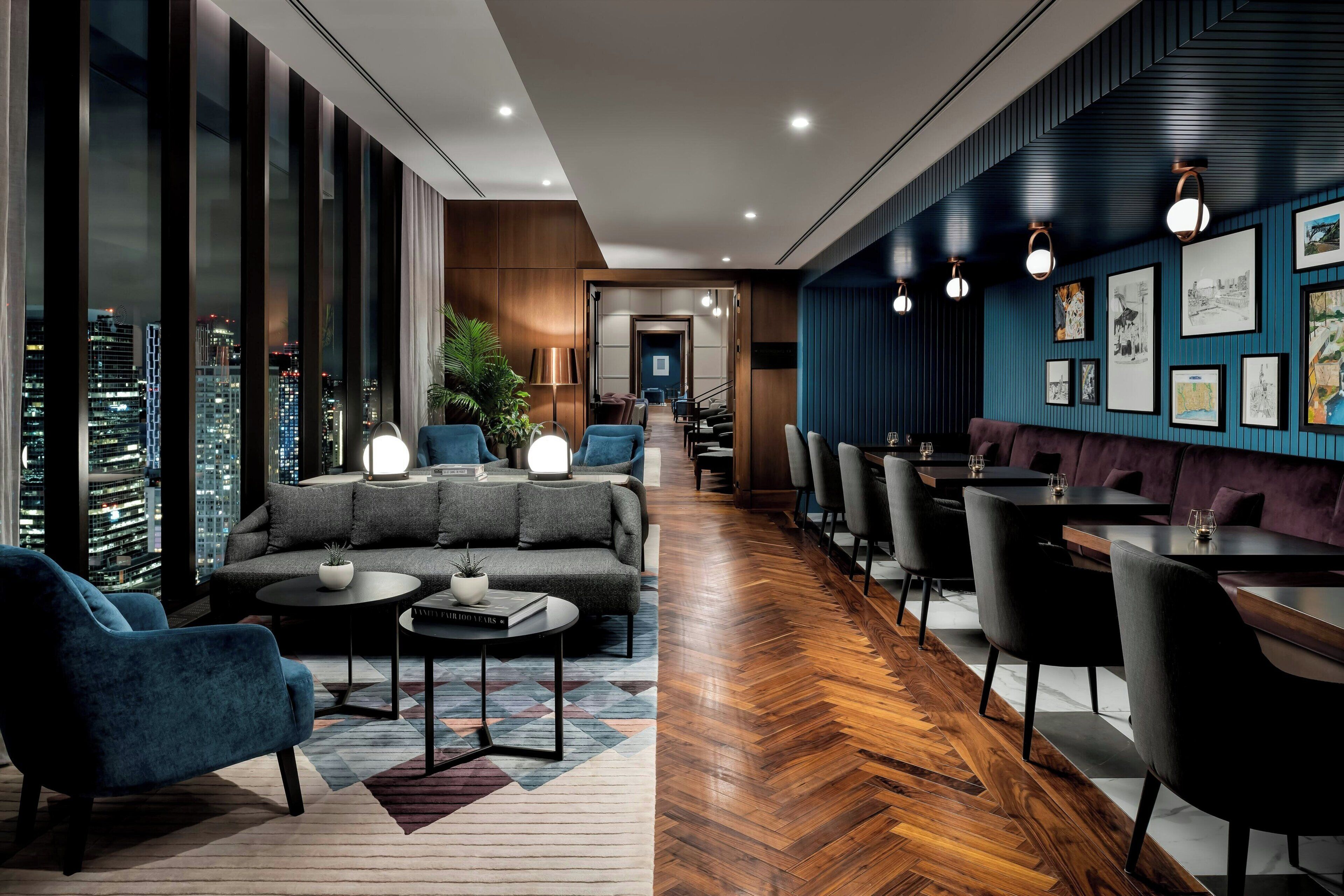 A modern hotel lobby with a sofa, armchairs, and a dining area.