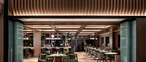 En modern restaurang med en bardel, grönt klädda sittplatser och en mönstrad matta.