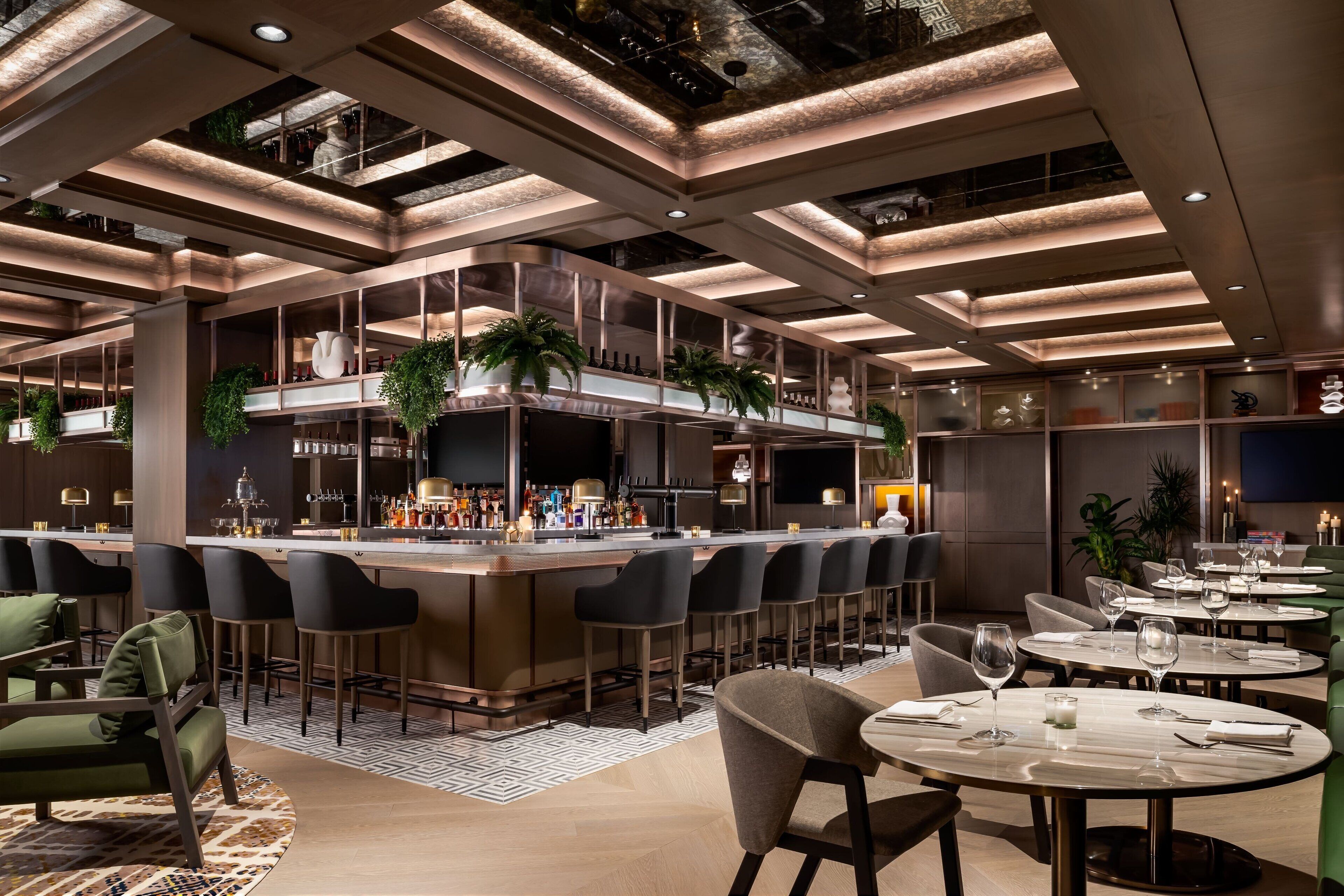 Un espace bar moderne doté d’un îlot central, de tabourets de bar et de tables rondes avec des chaises.