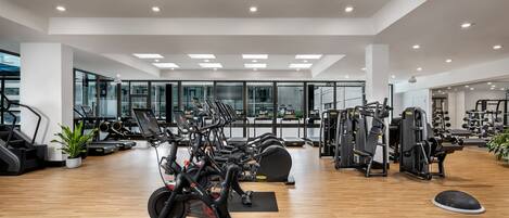 A modern gym with cardio machines, weightlifting equipment, and a wooden floor.