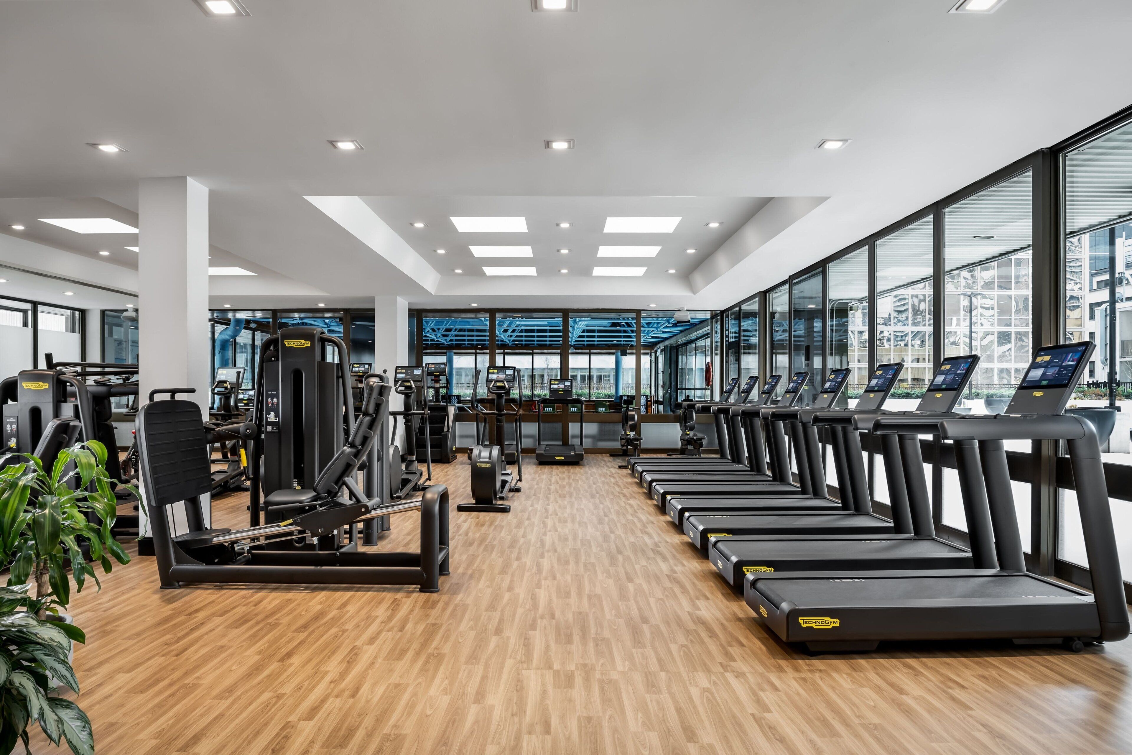 Une salle de sport moderne équipée de tapis de course, d’appareils de musculation et dotée d’une grande fenêtre offrant une vue sur la ville.