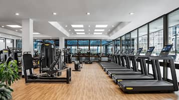Une salle de sport moderne équipée de tapis de course, d’appareils de musculation et dotée d’une grande fenêtre offrant une vue sur la ville.