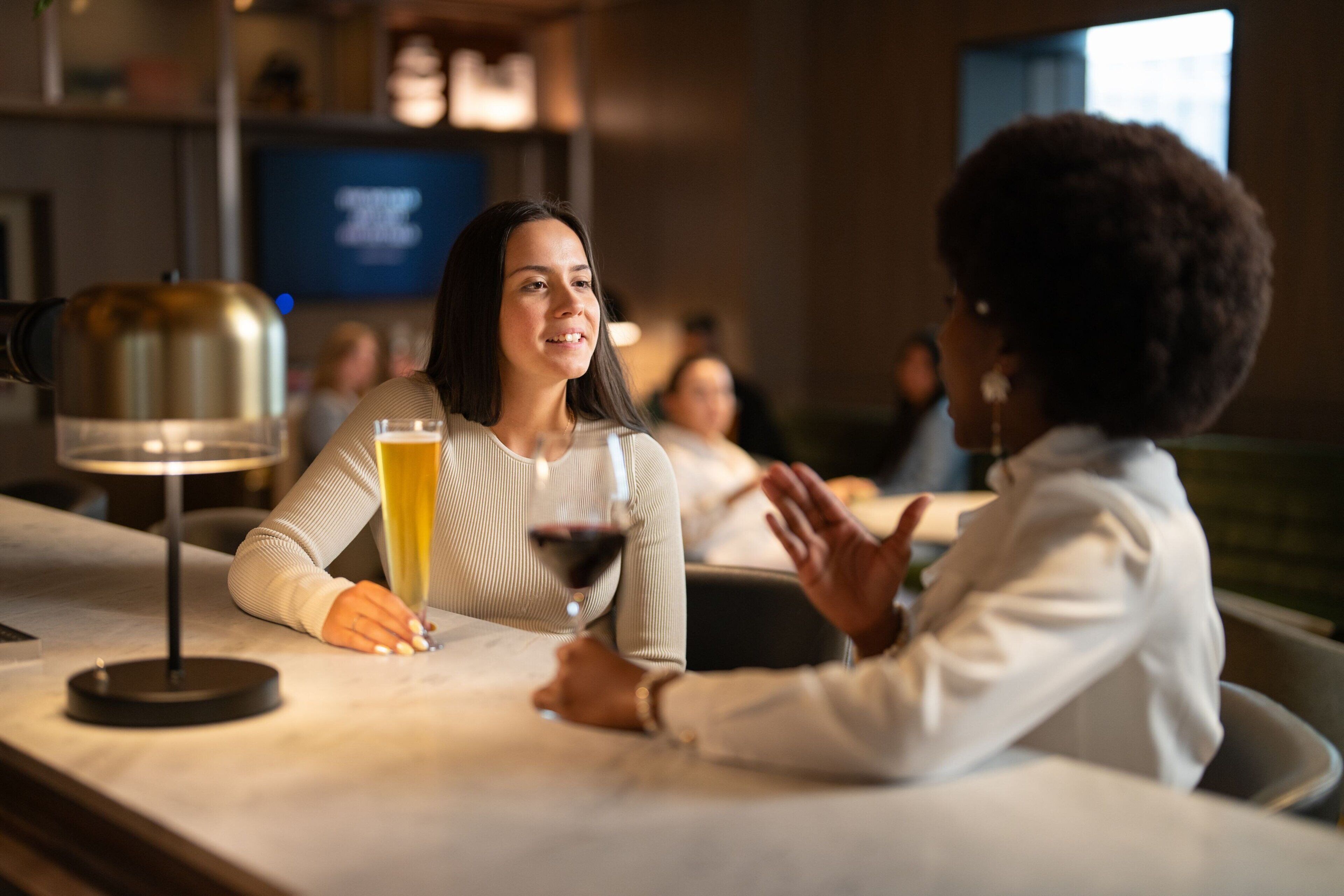 A bar setting with a person holding a glass of wine and another person gesturing.