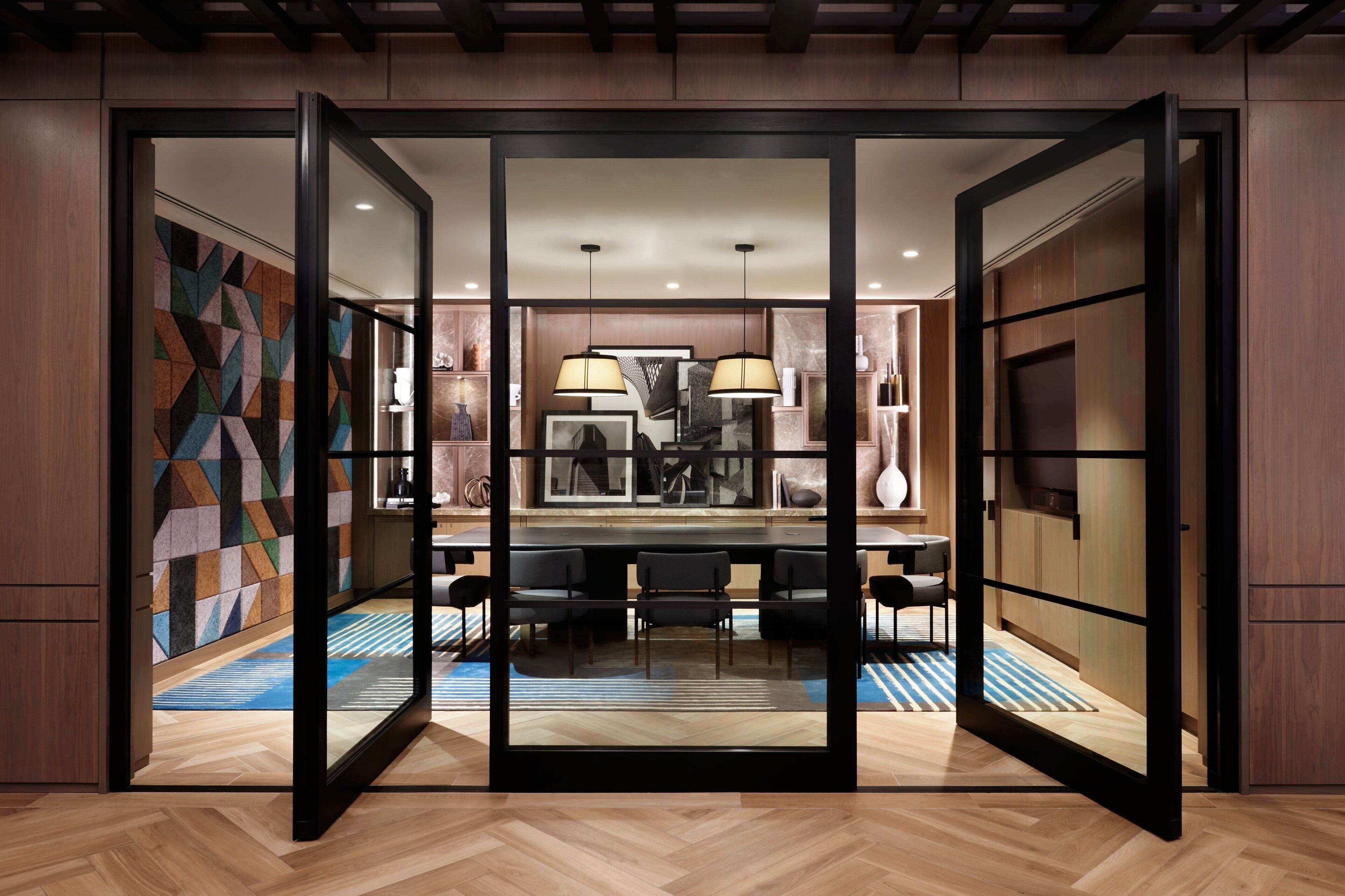 A modern interior with a wooden floor, a dining area with chairs, and a large mirror reflecting the space.