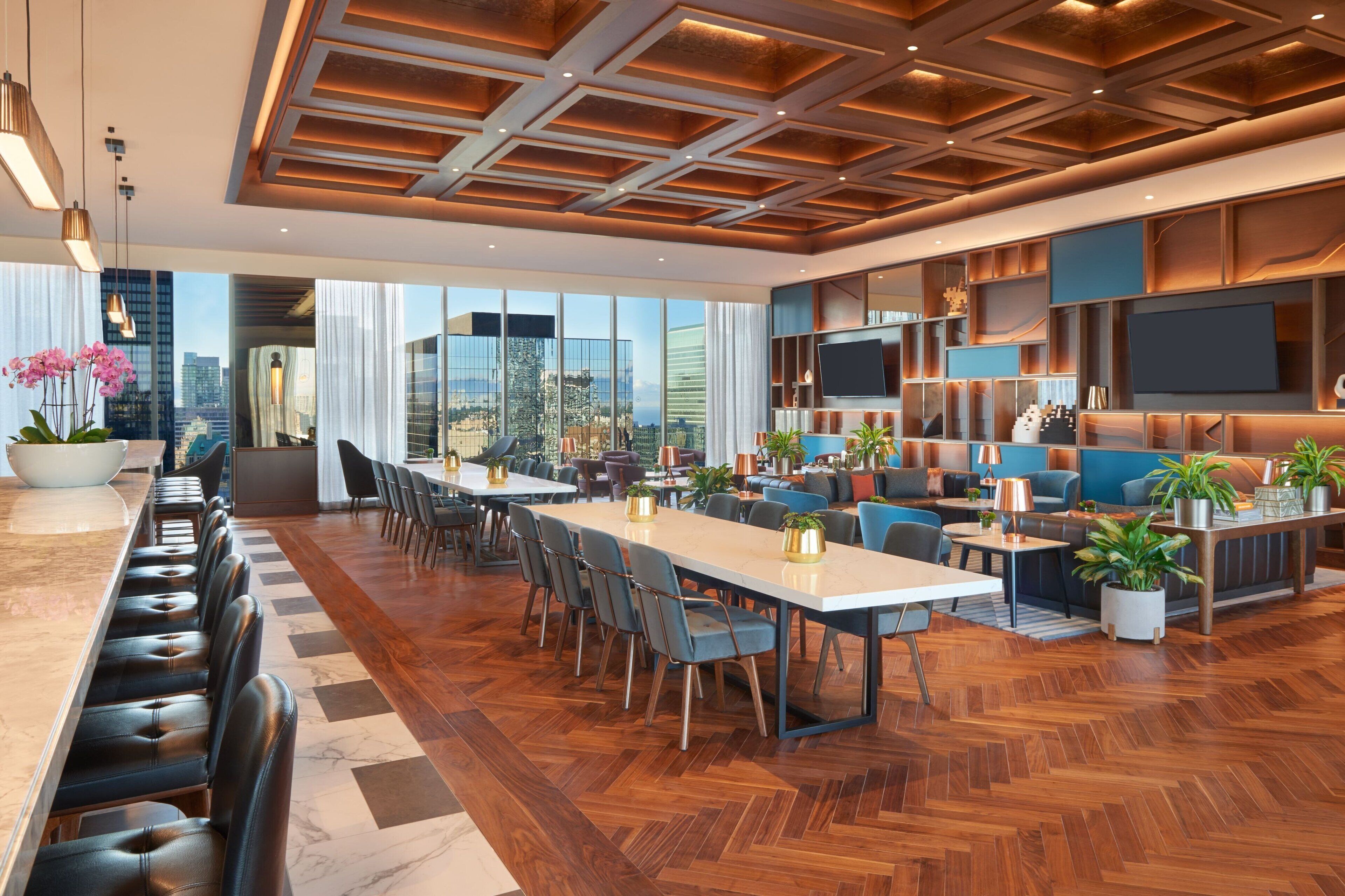 Un hall d’hôtel moderne avec un long comptoir d’accueil, un espace salon et un grand écran de télévision.