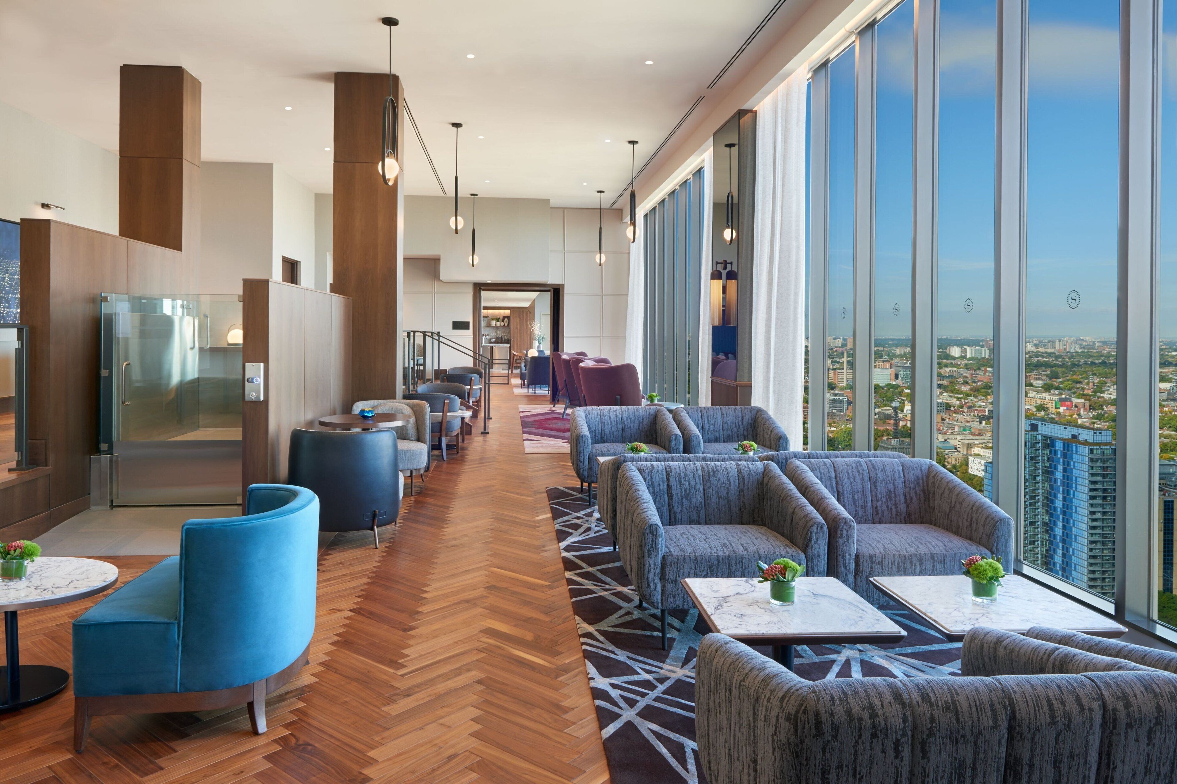 Eine moderne Hotelhalle mit hoher Decke, großen Fenstern mit Blick auf die Stadt und verschiedenen Sitzbereichen, darunter Sofas und Sessel.