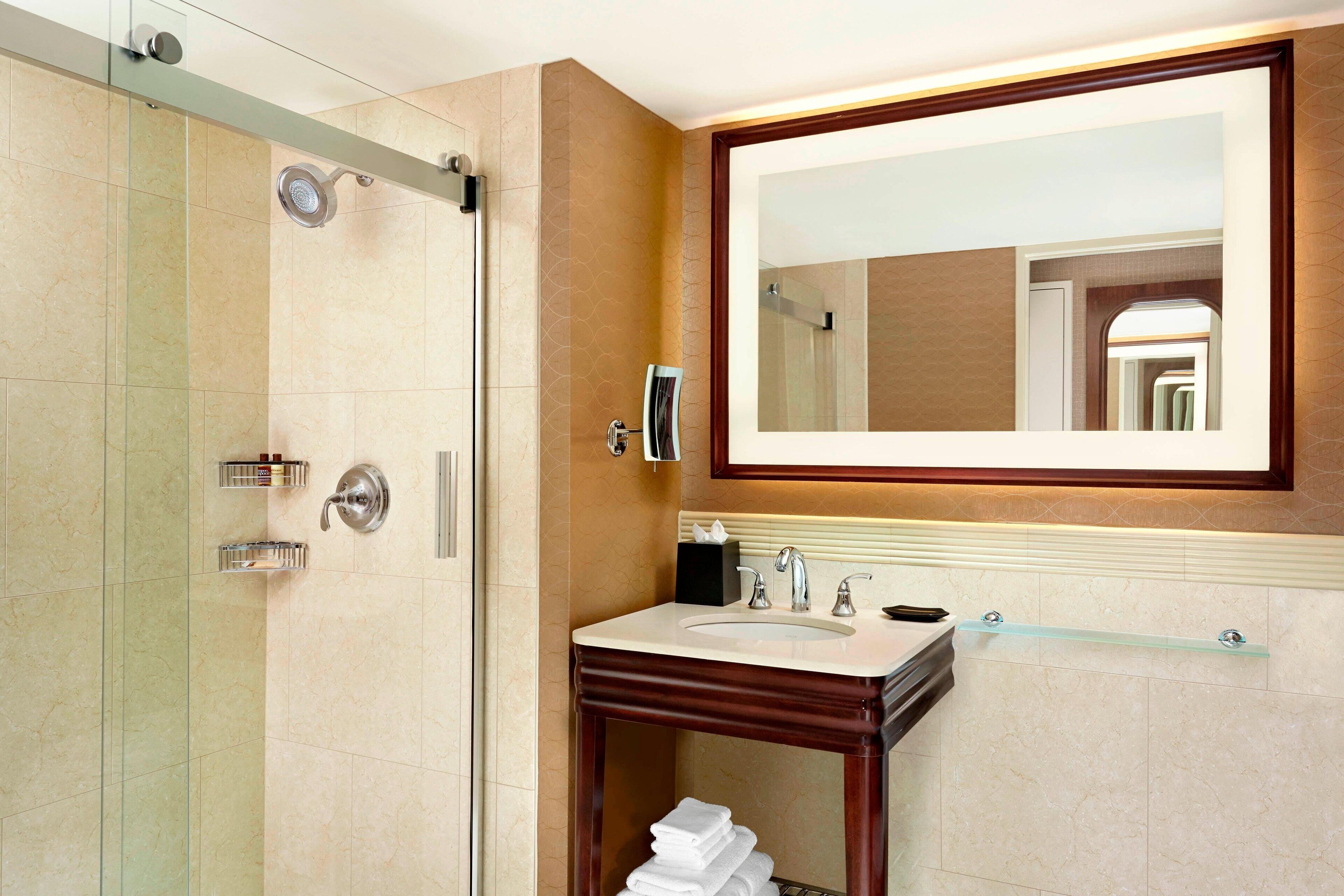 A modern bathroom with a glass shower enclosure, a vanity with a sink, and a large mirror.