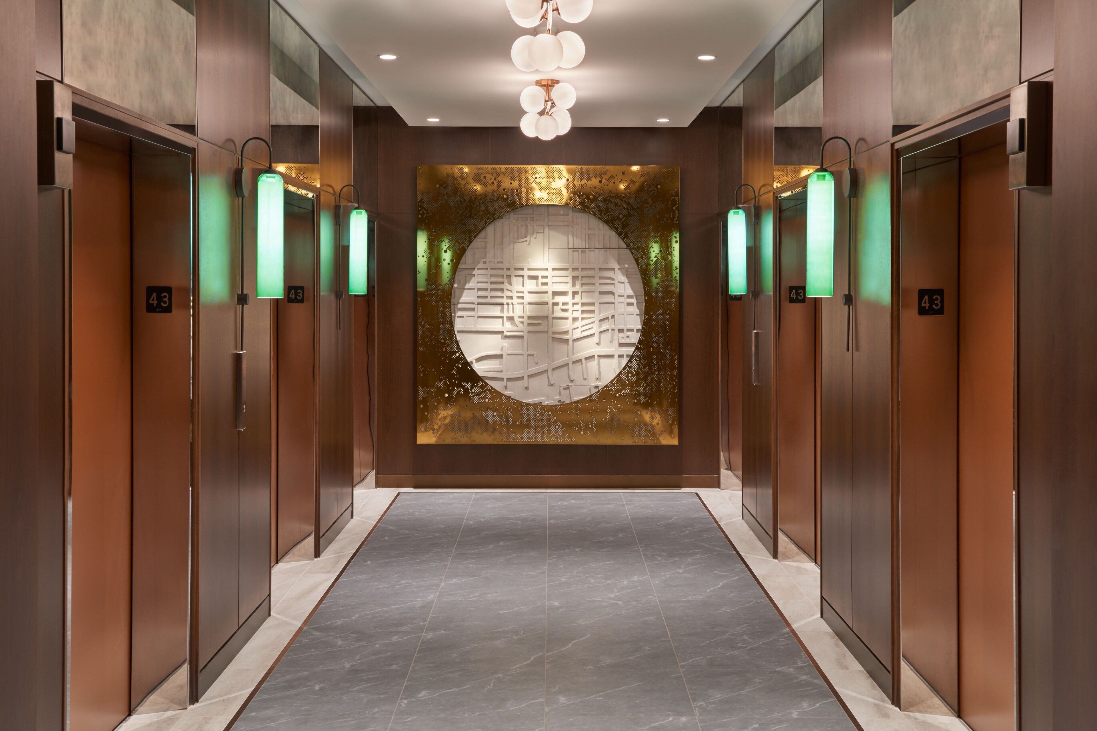A modern elevator lobby with a central decorative wall, multiple elevators, and a marble floor.