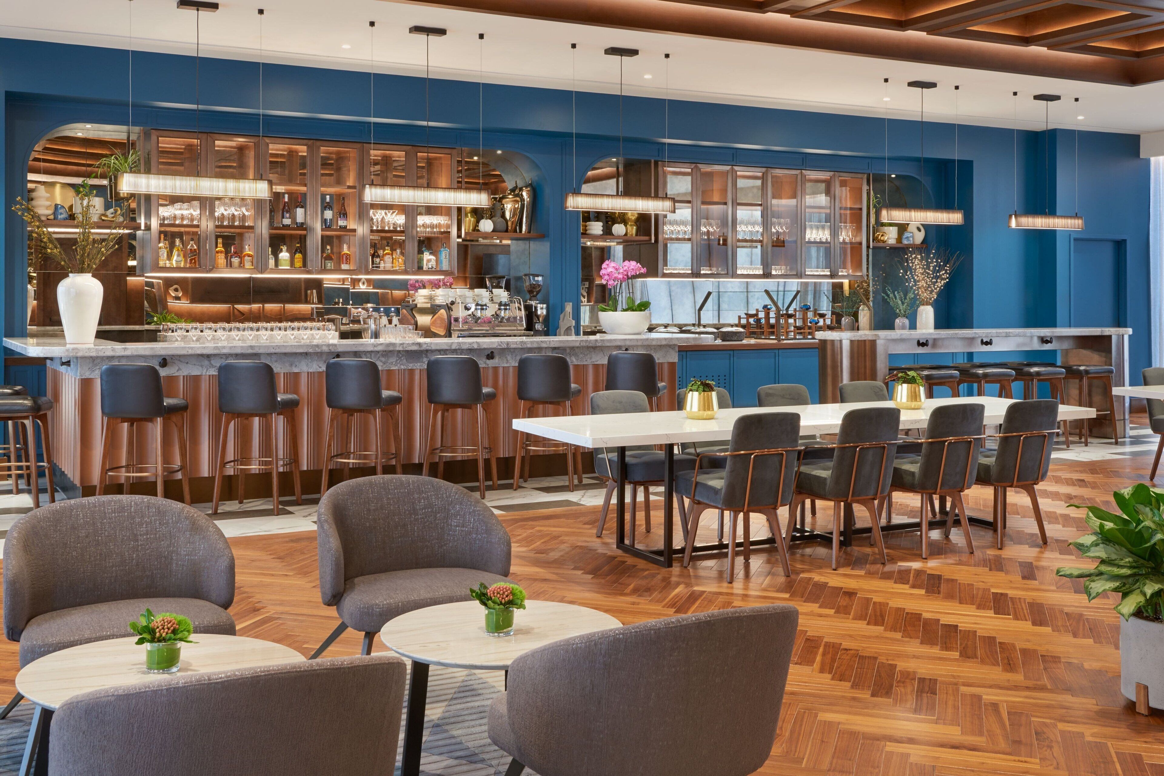 Un espace bar moderne doté d’un long comptoir, de plusieurs tabourets et d’un coin salon avec des tables et des chaises rondes.
