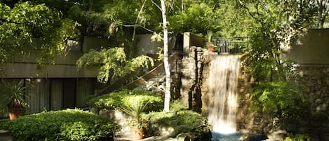 A waterfall in a landscaped garden with stone walls and potted plants.