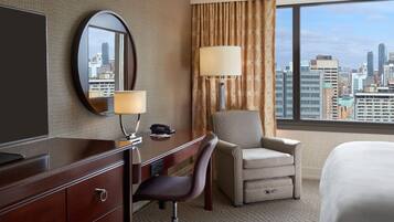Une chambre d’hôtel équipée d’un bureau, d’une chaise, d’un lit et d’une grande fenêtre donnant sur la ville.