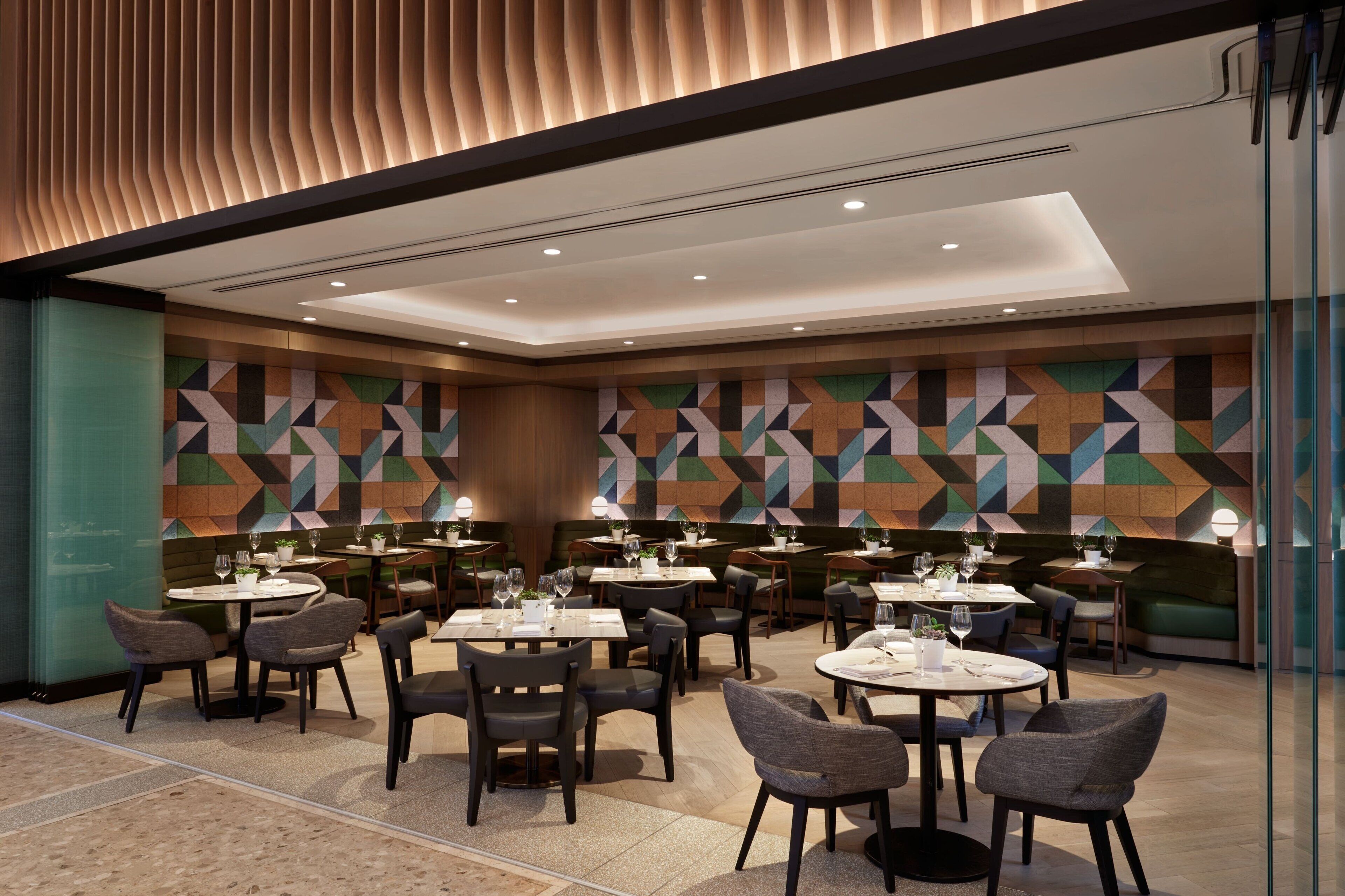 A modern dining area with multiple tables and chairs, geometric patterned walls, and recessed ceiling lighting.