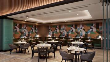 A modern dining area with multiple tables and chairs, geometric patterned walls, and recessed ceiling lighting.